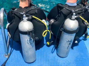 two men are sitting black diving suits with tubes metal oxygen tanks ready immersion