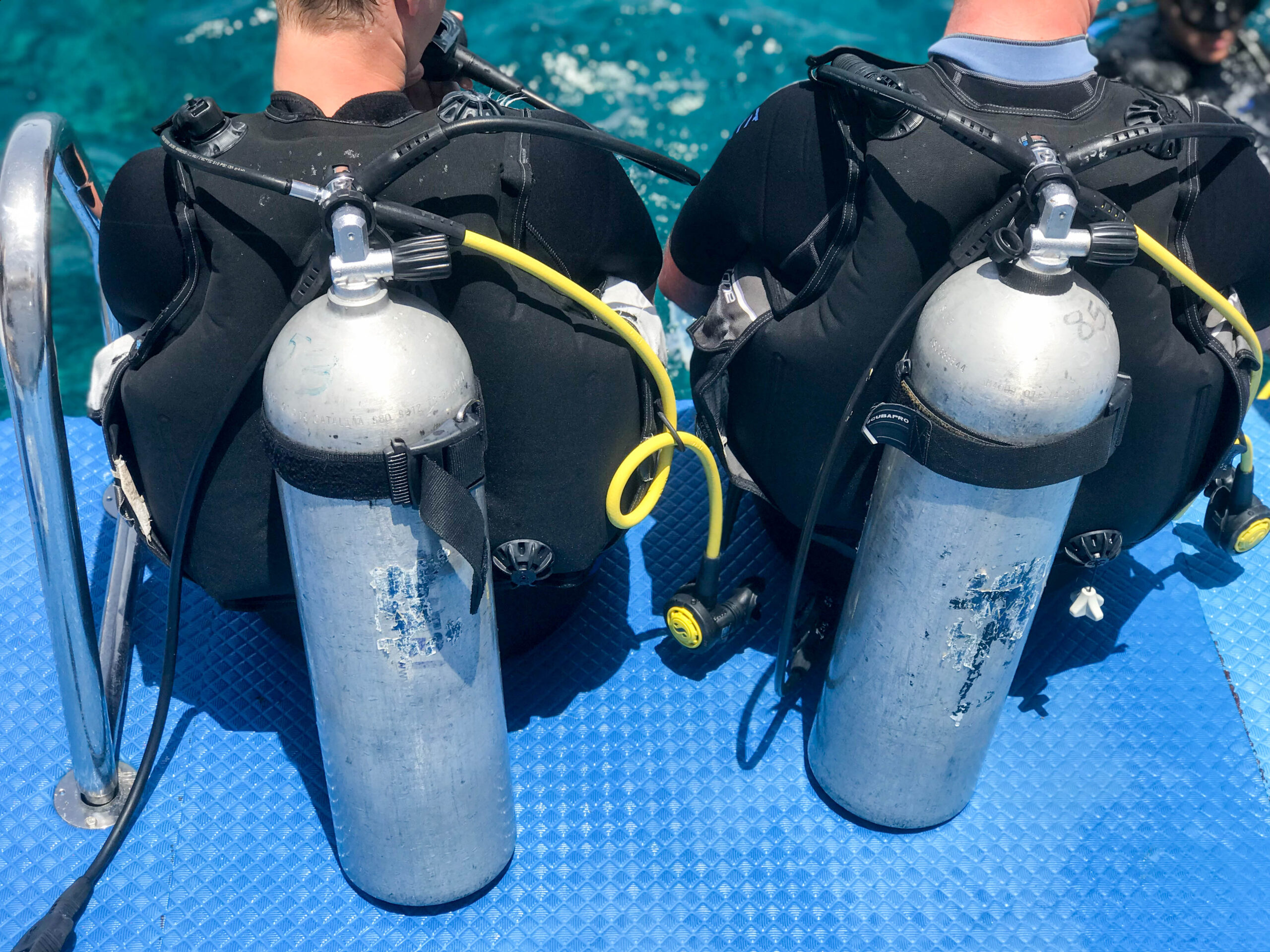 two men are sitting black diving suits with tubes metal oxygen tanks ready immersion